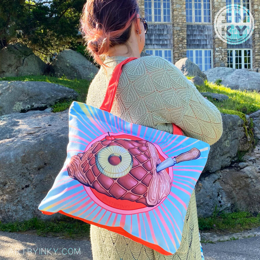 Person holding a large rum ham tote bag over their shoulder with rocks and a stone building in the background.